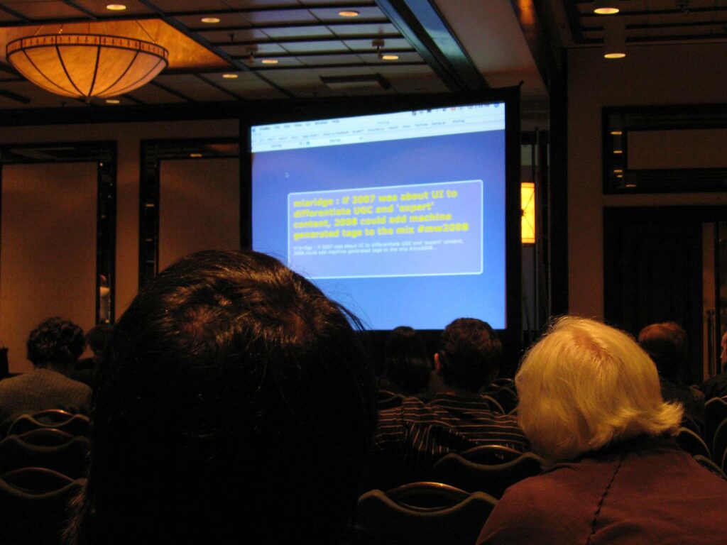 A slide projected in a 'fancy hotel'-style conference room. The text says: 'miaridge: if 2007 was about UI to differentiate UCG and 'expert' content, 2008 could add machine generated tags to the mix #mw2008'