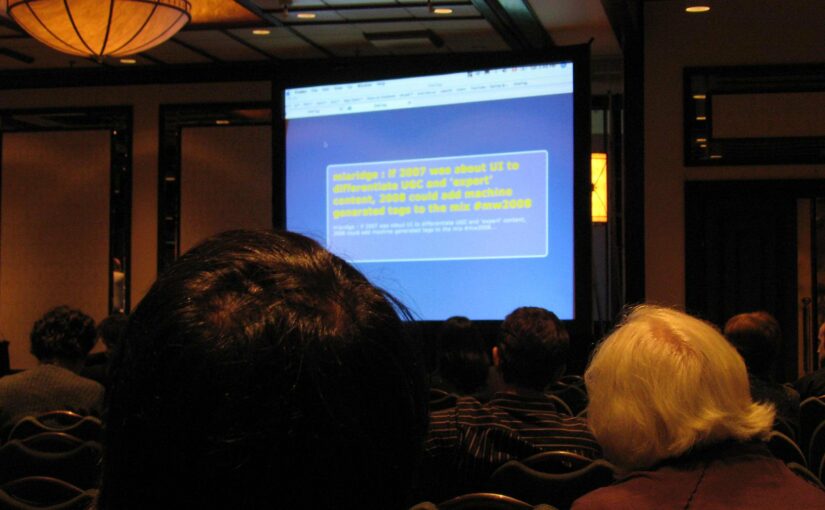 A slide projected in a 'fancy hotel'-style conference room. The text says: 'miaridge: if 2007 was about UI to differentiate UCG and 'expert' content, 2008 could add machine generated tags to the mix #mw2008'