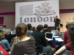 A photo of people in casual dress, lots of laptops, looking at a presentation 'Open Hack 2009 London'