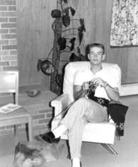 A 1950s black and white photo of a man knitting while relaxing in an armchair